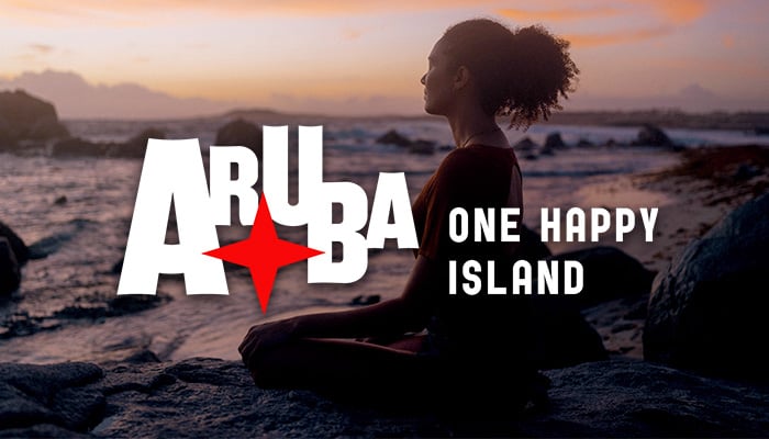 Woman sitting on a sandy beach at sunset, with the Aruba One Happy Island logo overlaid.