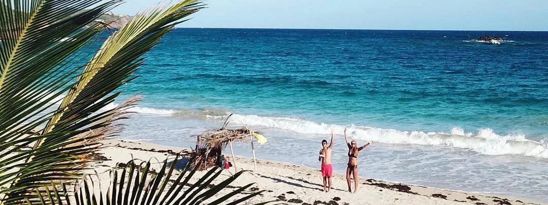 Couple on beach waving Antigua Caribbean